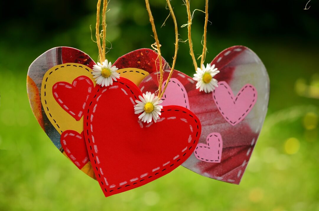 several red and pink hearts hanging together from threads, decorated by daisies