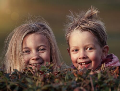 Two small smiling girls with wild hair peeking above a hedge
